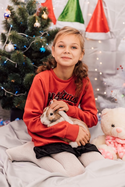 Nieuwjaar een meisje in een nieuwjaarstrui houdt een konijn bij de kerstboom