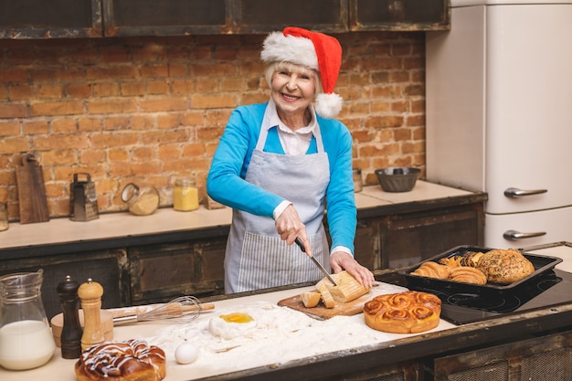Nieuwjaar koken. Het portret van aantrekkelijke hogere oude vrouw kookt op keuken. Grootmoeder die smakelijk Kerstmisbaksel maakt.