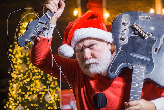 Foto nieuwjaar. slechte kerstman. kerstman met gebroken gitaar. kerstman kostuum. kersttijd. kerstmis. steen. elektrische gitaar.