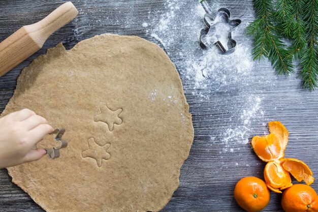 Nieuwjaars- en kerstversieringen op een houten oppervlak met mandarijnen en een kerstboom De handen van een klein kind maken mallen voor het koken van peperkoek in de vorm van een man