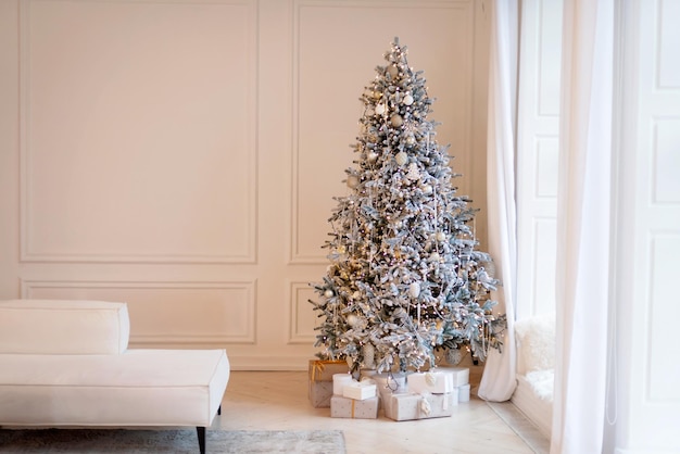 Nieuwjaarsboom is versierd met decoratieve ballen en bokehlichten, met kerstcadeaudozen bij het raam in de lichte kamer. Zachte selectieve focus.