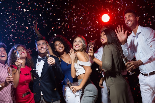 Nieuwjaarsfeest. Groep vrienden glimlachend en handen naar boven schuddend, nachtclubreportage