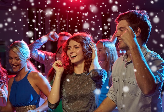 nieuwjaarsfeest, vakantie, feest, nachtleven en mensenconcept - groep gelukkige vrienden die dansen in nachtclub en sneeuweffect