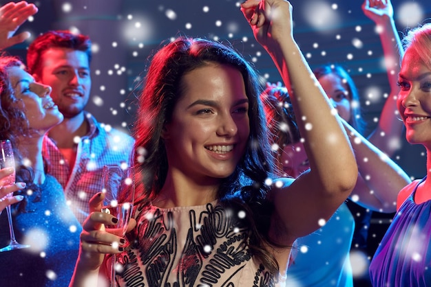 nieuwjaarsfeest, vakantie, feest, nachtleven en mensenconcept - lachende vrienden met glazen niet-alcoholische champagne dansen in club en sneeuweffect