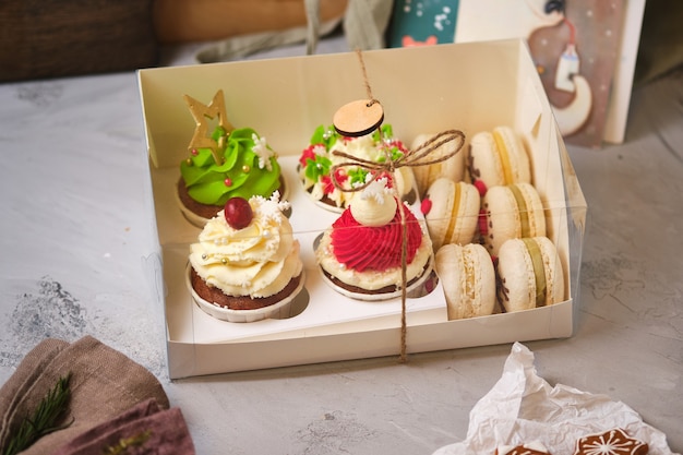 Nieuwjaarsgeschenksets met snoep. Een doos cupcakes en macarons als kerstcadeau. Cupcakes met roomkaasroom en pinda-karamel vulling en macaronscakes met mandarijnvulling.