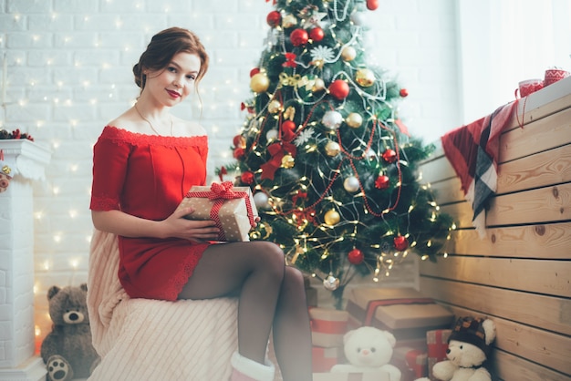 Nieuwjaarsmeisje met een cadeau in haar handen bij de kerstboom