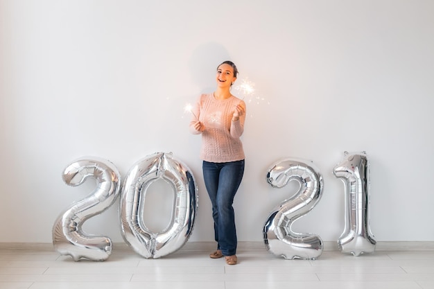 Nieuwjaarsviering en feestconcept - gelukkige jonge vrouw met sterretjes in de buurt van zilveren 2021-ballonnen op witte achtergrond.