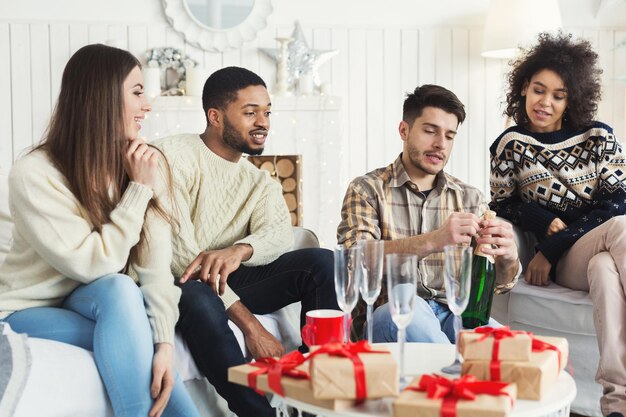 Nieuwjaarsviering. Jonge man knalt kurk uit champagnefles voor vrienden, kopieer ruimte