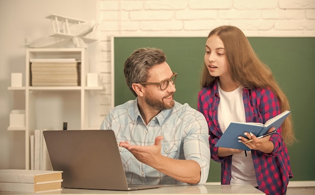 Nieuwsgierig tienermeisje en leraar man op de middelbare school met werkboek en pc bij schoolbord ouderschap