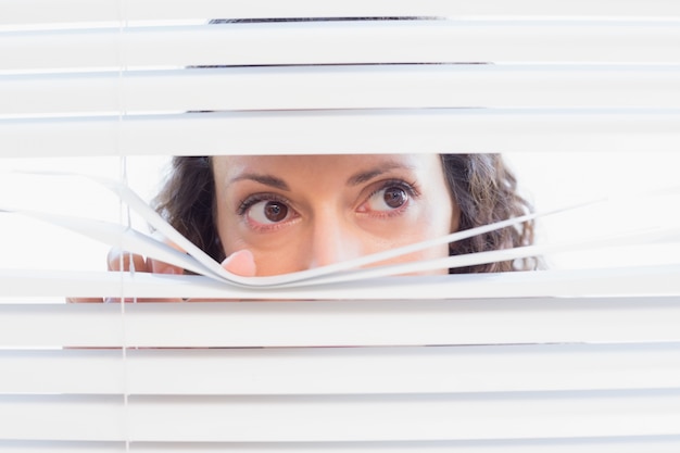 Nieuwsgierige vrouw die door zonneblinden kijkt