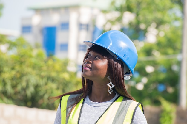 A Nigerian female construction and architectural engineer giving thumbs up with a blue safety helmet