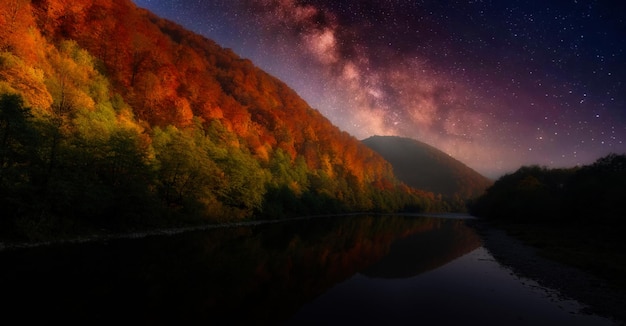 Night in the autumn mountains Starry sky yellow leafy trees and fog