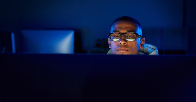 Night black man or hacker reading on computer for cybercrime malware or phishing for stealing online data Programmer face and software update on pc for hacking scam or theft on website in dark