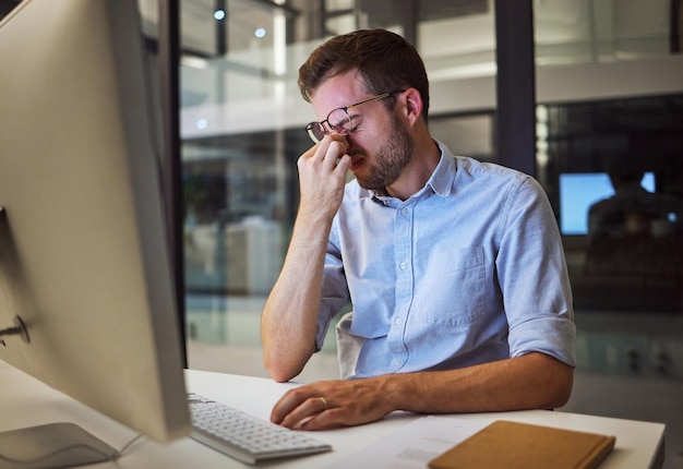 Night business stress and tired man sitting at his computer desk with headache depression and burnout from work pressure Stressed mental health and depressed male working late in his office