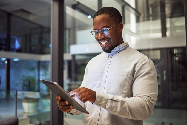 야간 비즈니스 태블릿과 흑인 남성이 온라인으로 정보를 입력하고 읽고 연구를 하고 늦게까지 일하는 좋은 결과에 미소를 짓고 있습니다. 나이지리아 사무실에서 마케팅 전략을 위해 인터넷에서 행복한 남성
