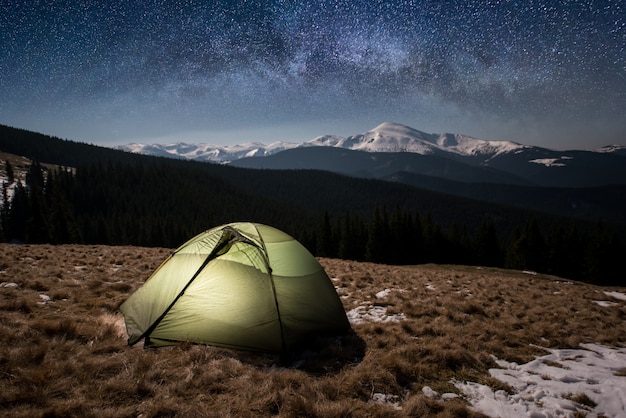 夜のキャンプ。星と天の川でいっぱいの美しい夜空の下で照らされた観光テント