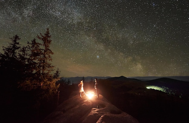 夜の星空の下でキャンプファイヤーの周りの人々との夜のキャンプ