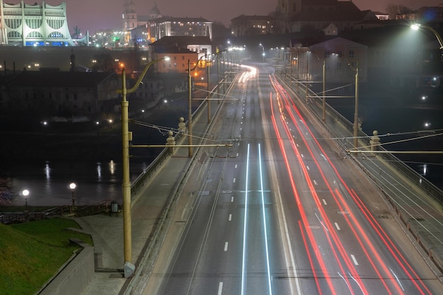 夜の街通りの光の道遅いシャッタースピードの写真川を渡る長い橋が大都会に通じる町の中心部にあるにぎやかな高速道路