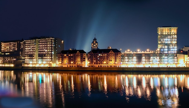 The night city stands on the river and the lights of the windows can be seen in the reflecti