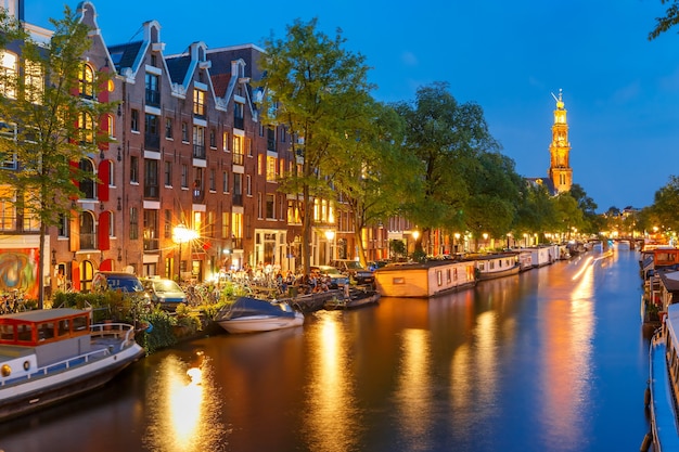 Night city view of Amsterdam canal Prinsengracht with houseboats and Westerkerk church, Holland, Netherlands.