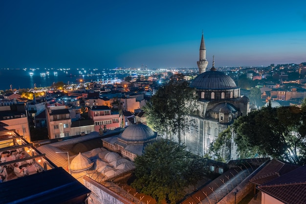 Night cityscape with buildings rooftop restaurant mosque minaret and lights in sea Istanbul Turkey