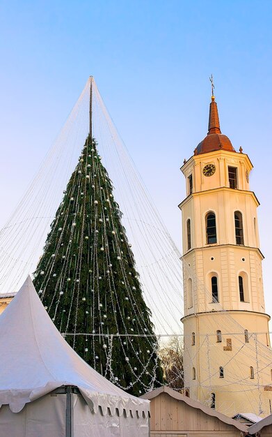 Night Cityscape with Christmas Market at Cathedral square in Winter Vilnius, Lithuania. Advent Fair Decoration and Stalls with Crafts Items on the Bazaar. Lithuanian street Xmas and holiday