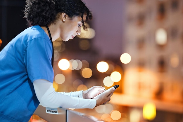 Night doctor and woman texting in city while on a break internet and search against a bokeh background Nurse female and online app for schedule calendar and planner while relaxing on a balcony