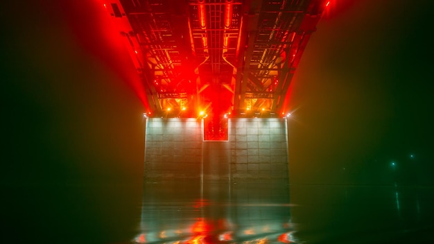 Night foggy view of the illuminated pillar of the bridge over the river