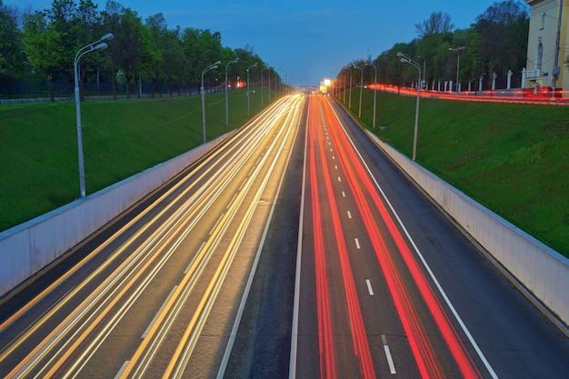 車のライトが付いている夜の高速道路。スピードトラフィックのある道路の黄色と赤のライトトレイル。長時間露光抽象的な都市の背景