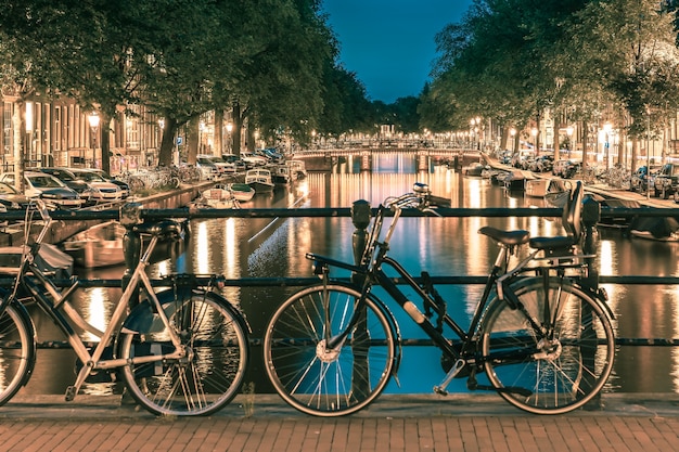 Night illumination of Amsterdam canal and bridge with typical dutch houses, boats and bicycles, Holland, Netherlands.. Toning in cool tones