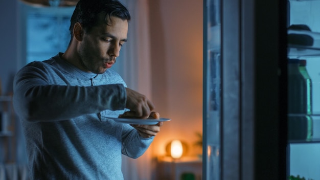Photo at night in the kitchen handsome attractive young man is eating a leftover pizza from the fridge he is hungry and feels satisfied