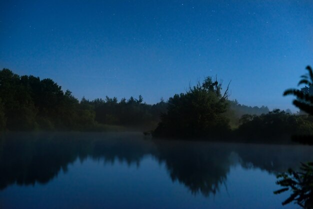 Night on the lake with dark blue water and stars on the sky