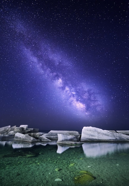 Foto paesaggio notturno con colorata via lattea al mare con pietre. cielo stellato. spazio sullo sfondo