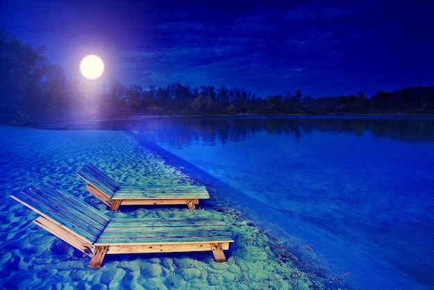 Night landscape with two wooden sunbeds bank of lake in the night in autumn