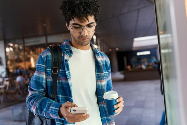 Ночной портрет задумчивого ближневосточного мужчины с помощью мобильного телефона, держащего чашку кофе, проверяющего электронную почту