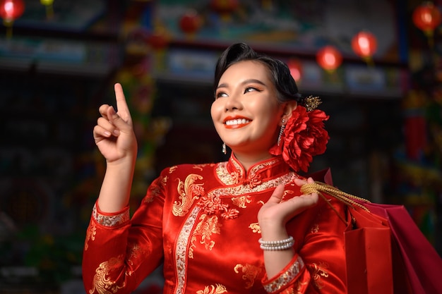 夜のシーン、中国の旧正月の神社で笑顔と買い物袋でポーズをとってチャイナドレスを着て肖像画アジアの美しい女性