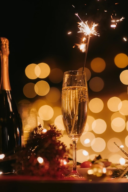 Photo night shot of flute with champagne and sparkler with warm bokeh and atmosphere of new year eve