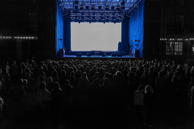 Night show performance. Many people waiting for the night show near the scene with big white screen.