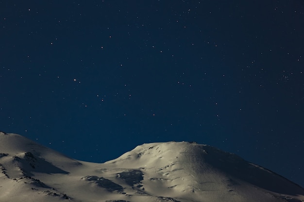 Night sky with bright stars over the peaks of Mount Elbrus. Snow-covered peaks of a stratovolcano in the North Caucasus in Russia.