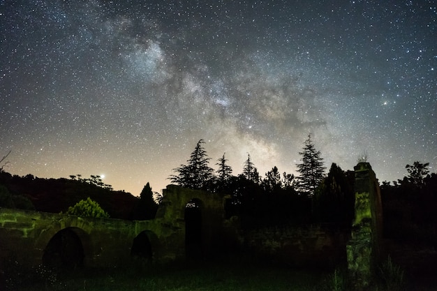 Night sky with Milky Way above forest and ruins in Spain