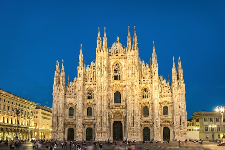 Фотография ночной вид на знаменитый миланский собор (duomo di milano) на площади в милане, италия со звездами на синем темном небе