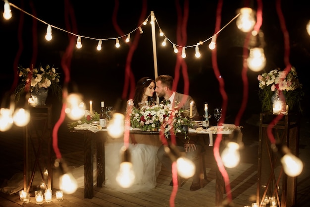 밤의 결혼식. 신랑 신부가 축제 테이블에 앉아 있습니다. 연회