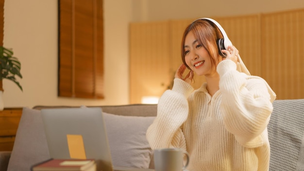 나이트 라이프 개념 겨울 밤에 노트북에서 음악을 듣기 위해 헤드폰을 끼고 있는 젊은 여성