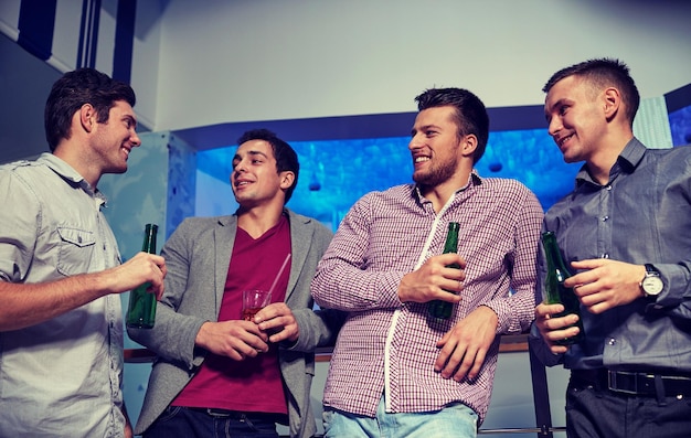 밤문화, 파티, 우정, 여가, 그리고 사람들의 개념 - 나이트클럽에서 맥주병을 마시고 웃고 있는 남자 친구들
