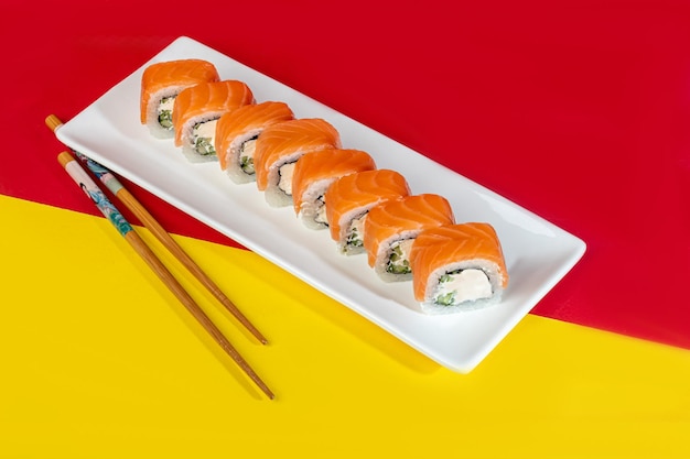 Nigiri sushi sets Uramaki California Philadelphia op een witte plaat In de buurt van gember en wasabi Sojasaus in een witte kom Op een gekleurde achtergrond
