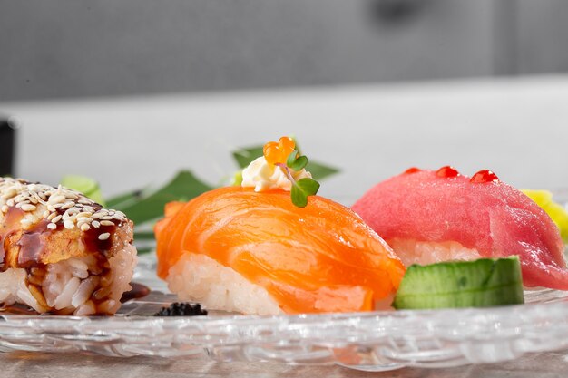 Nigiri sushi with salmon, eel, tuna and prawn, served on transparent plate.