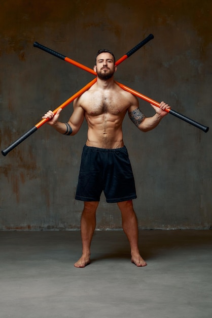 A ninja man holds on to a fighting stick and attacks closeup on gray studio background