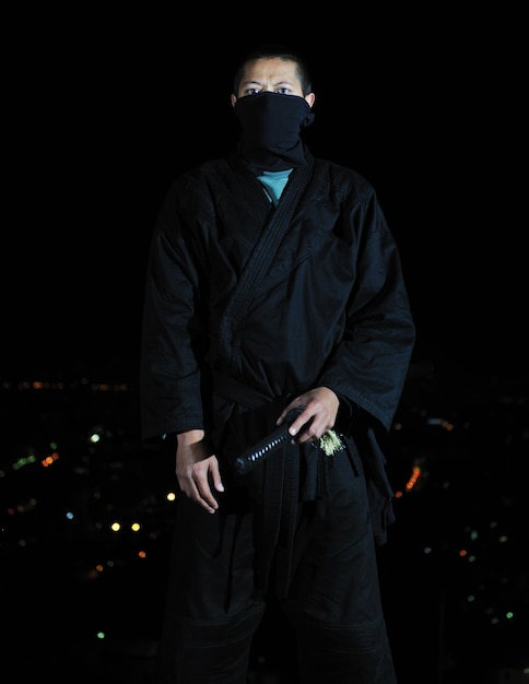 Ninja moordenaar houden katana samurai oude krijgskunst wapen zwaard nacht met stad lichten op de achtergrond