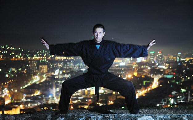 Ninja moordenaar houden katana samurai oude krijgskunst wapen zwaard nacht met stad lichten op de achtergrond