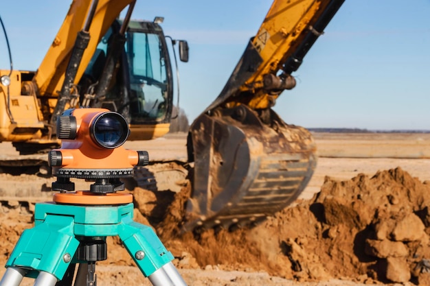 Niveau met een graafmachine op de achtergrond Bouwniveau of theodoliet Geodetische instrumenten en apparatuur voor de bouw en grondwerken